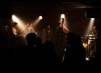 Audience watching a band with brass instruments, double bass and drums in a small venue