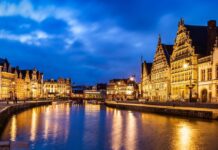 Ghent by train from the UK: how to plan a relaxed two-night city break Illuminated buildings along Graslei and Korenlei reflected in the river in Ghent at dusk